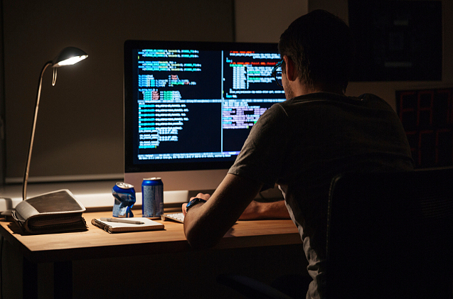 Back view of modern programmer sitting and writing code in dark room