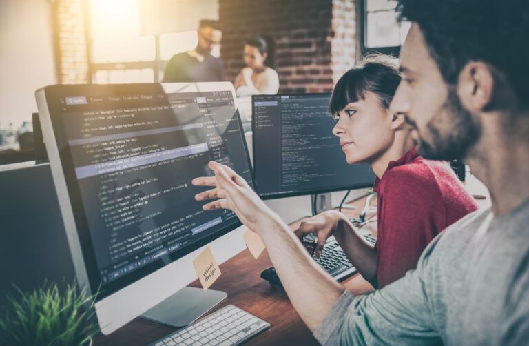 Dos profesionales TI trabajan en una oficina (Adobe).